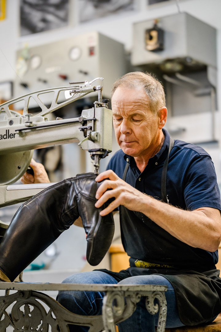 Schuhmacher bei Reparatur eines Schuhs in der Werkstatt mit einer Maschine zu sehen.